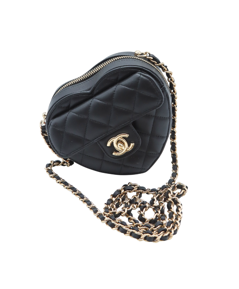 Black quilted Chanel heart-shaped handbag with gold chain strap on a white background